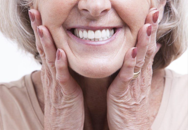 Elderly woman with dentures, smiling, with her ands on her cheek